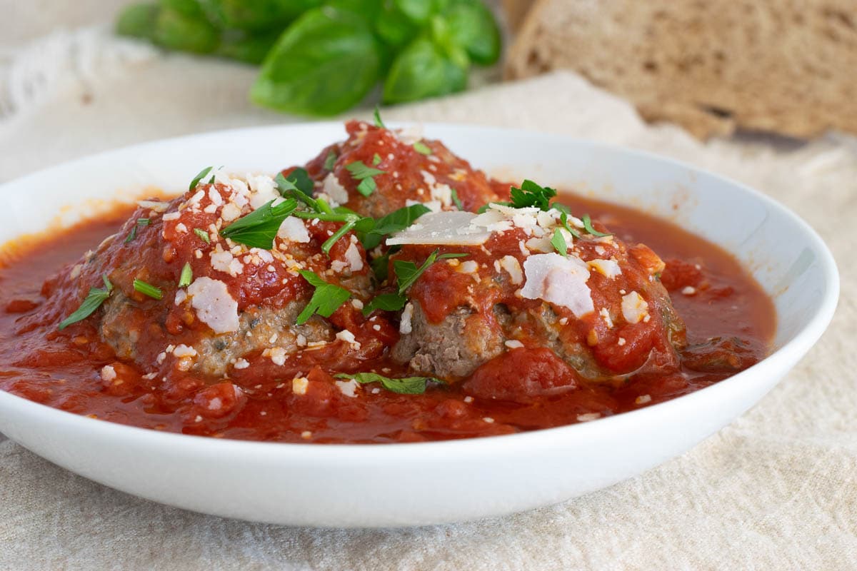 Three meatballs in a bowl of marinara sauce.