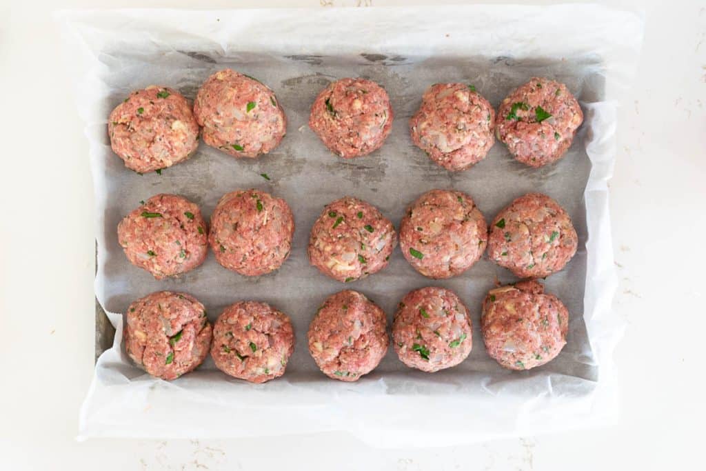Raw meatballs on a rimmed baking sheet.