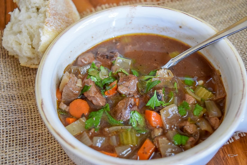 A bowl of hearty beef soup and a spoon.