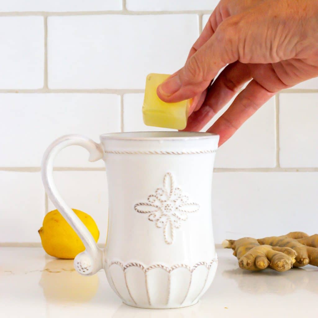 Adding a ginger lemon tea cube to a cup of hot water.