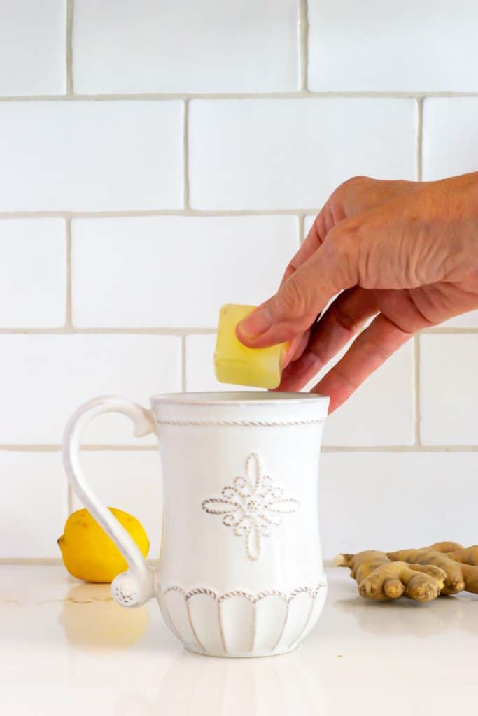 Adding a ginger lemon tea cube to a cup of hot water.