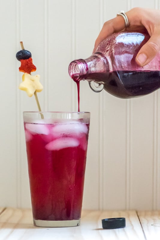 hand pouring blueberry syrup in a glass.