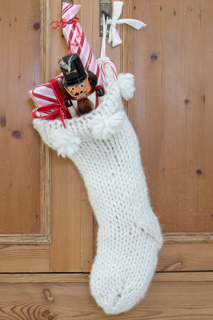 Knit Christmas stocking with nutcracker and small presents inside.