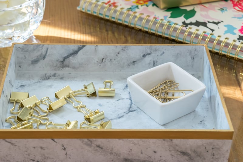 A rectangular marble tray with gold clips and gold paperclip.