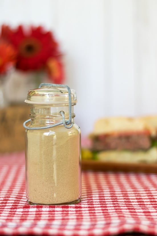 Our recipe for the perfect Hamburger Seasoning. Full Bottle of hamburger seasoning sitting on table - burger in the background 