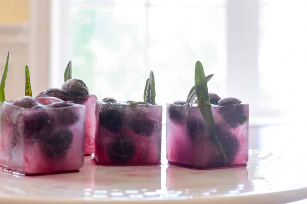 Ice cubes with blueberries and rosemary petals frozen inside.