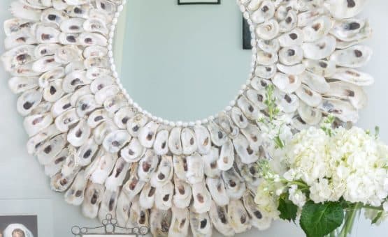 Oyster Shell Mirror on a wall with a vase of flowers.