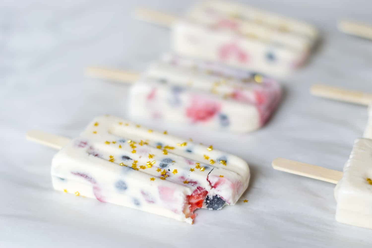 EASY to make red, white and blue ice cream popsicles are perfect for your Fourth of July festivities. Vanilla ice cream, chopped fresh strawberries and fresh blueberries make a perfect ice cream popsicle, made even more perfect with edible gold star sprinkles to up the 4th of July fun.