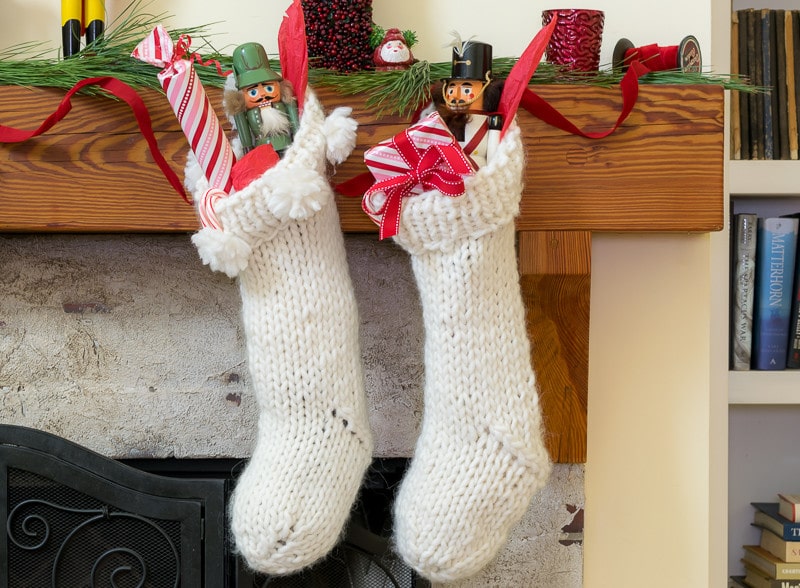 Two filled knit Christmas stockings hanging from a mantel.