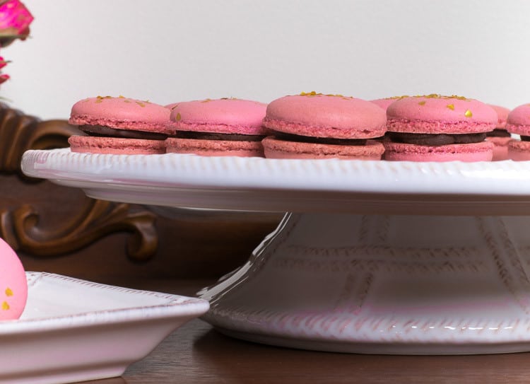 Sideview of raspberry macarons with chocolate ganache on cake stand