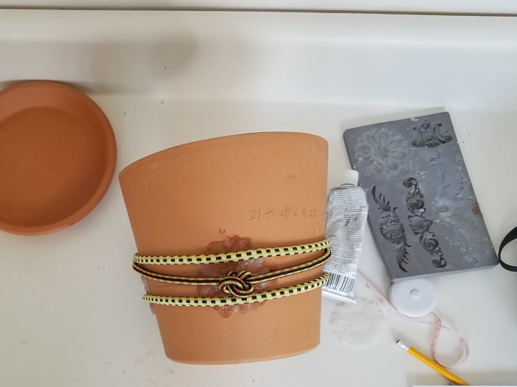 using bungee cords to hold diy flexible medallion on pot while the glue dries