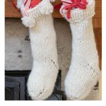 2 White Knit Christmas STockings filled, hanging on mantle