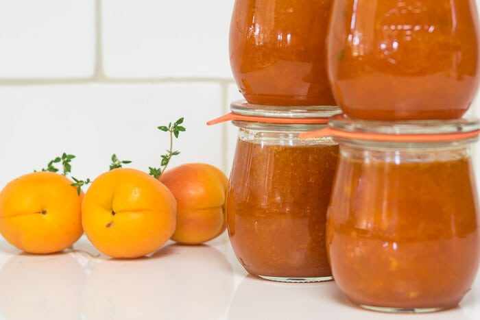 Jars of Apricot Jam with fresh apricots and thyme in the background.