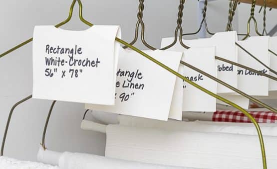 Table Linens haning in closet, labeled with size and description