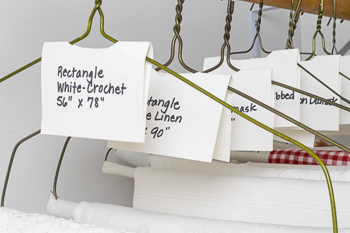 Table Linens haning in closet, labeled with size and description