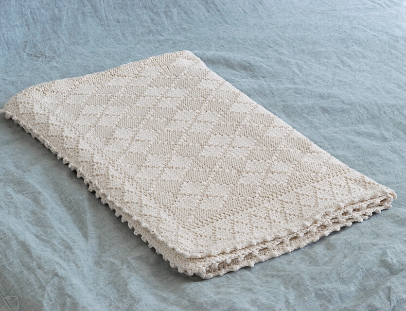 Beige knit baby blanket on a blue bedspread.