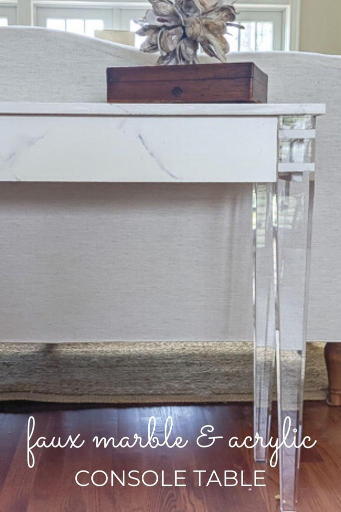 console table with acrylic legs and a faux marble top with white sofa in the background.
