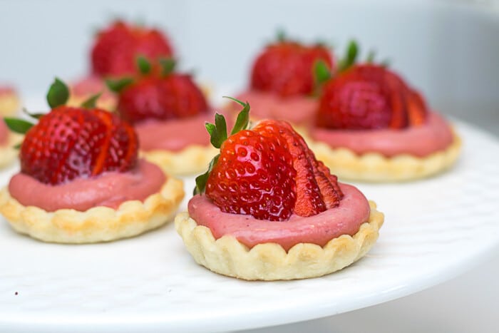 Strawberry Mini Tarts, with a fanned strawberry topping them, on a white platter.
