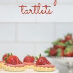 strawberry tartlets on a cake stand with strawberries in the back.