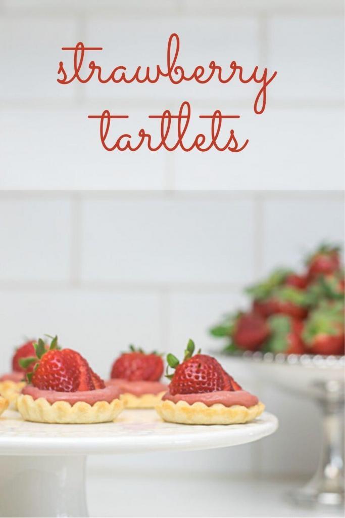 strawberry tartlets on a cake stand with strawberries in the back.