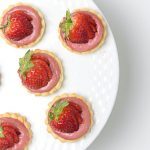 overhead of strawberry tartlets on a cake plate.