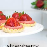closeup of strawberry tartlets on white cake plate.