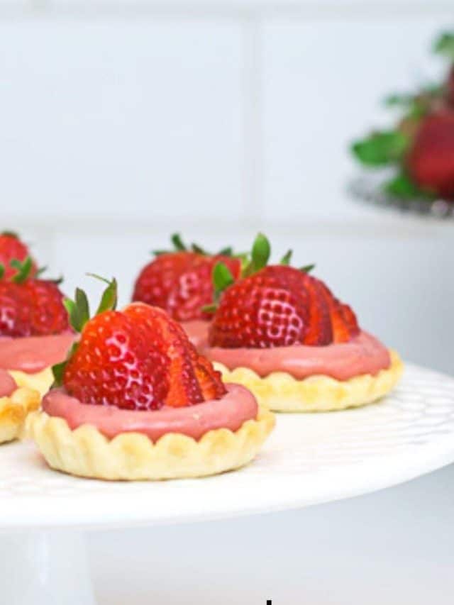 closeup of strawberry tartlets on white cake plate.