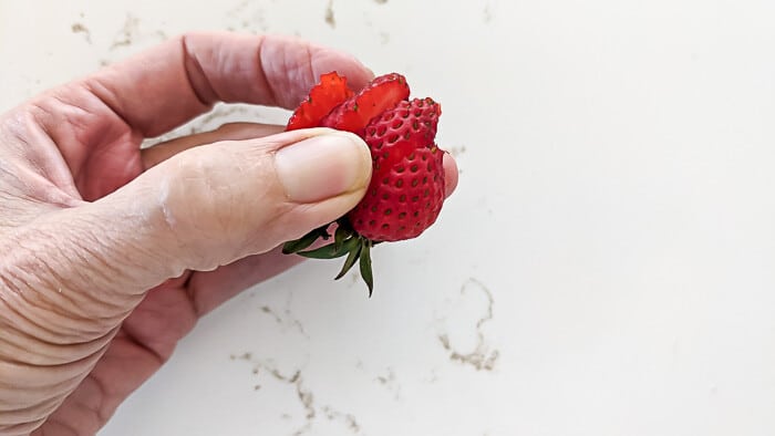 A cut and fanned strawberry to top the strawberry tartlets.