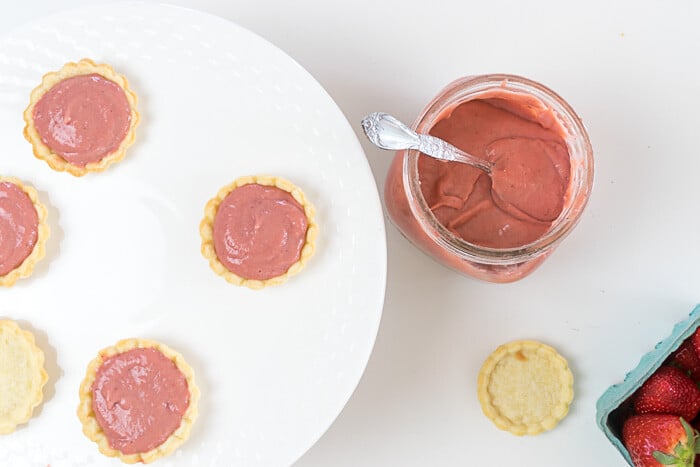 Jar of strawberry curd and strawberry curd in tarts, overhead shot.
