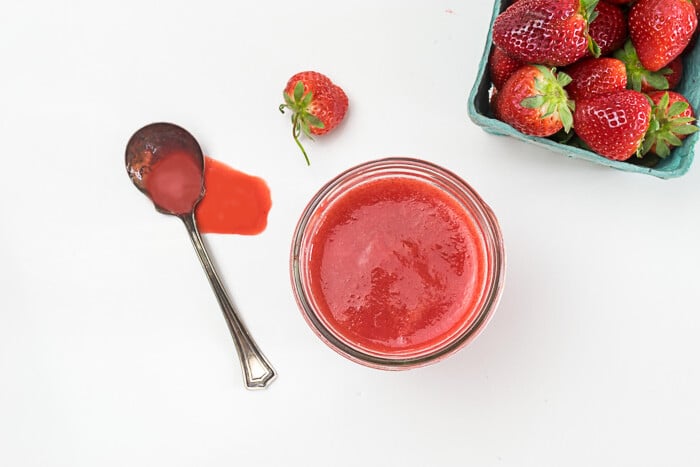 Overhead shot of strawberry puree, with spilled puree on counter and some fresh strawberries.