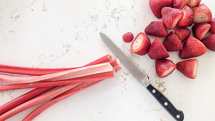stalks of rhubarb and a pile of strawberries on a counter next to a knife.
