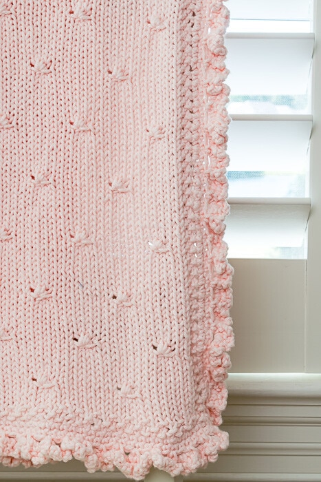 Finished Pink Knit Baby Blanket Pattern hanging over a chair, against a window.