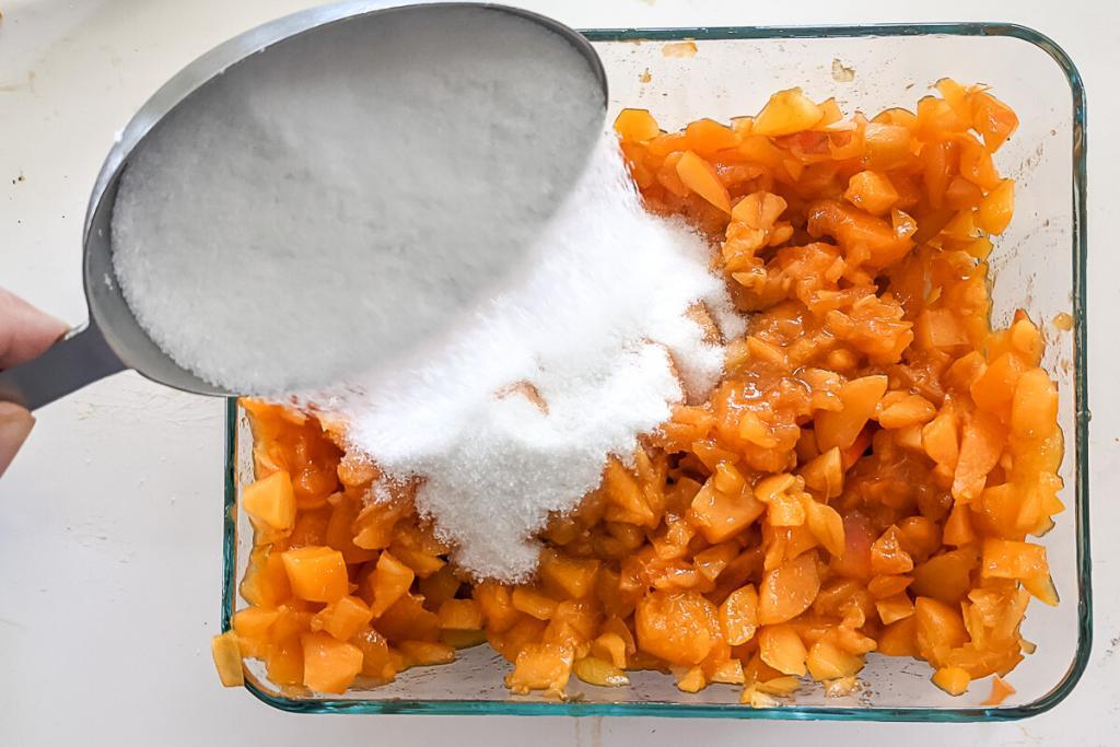 Adding sugar to the mashed apricots in preparation for macerating the apricots.