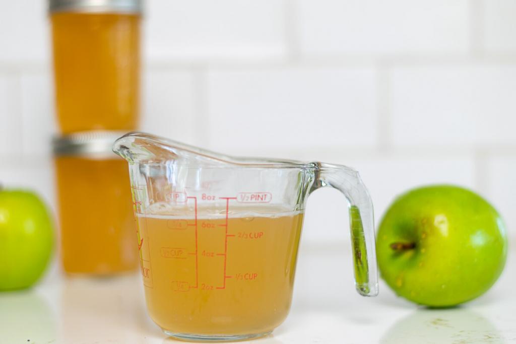 Measuring cup filled with Apple Pectin Stock with 2 jars of pectin stock in the background.