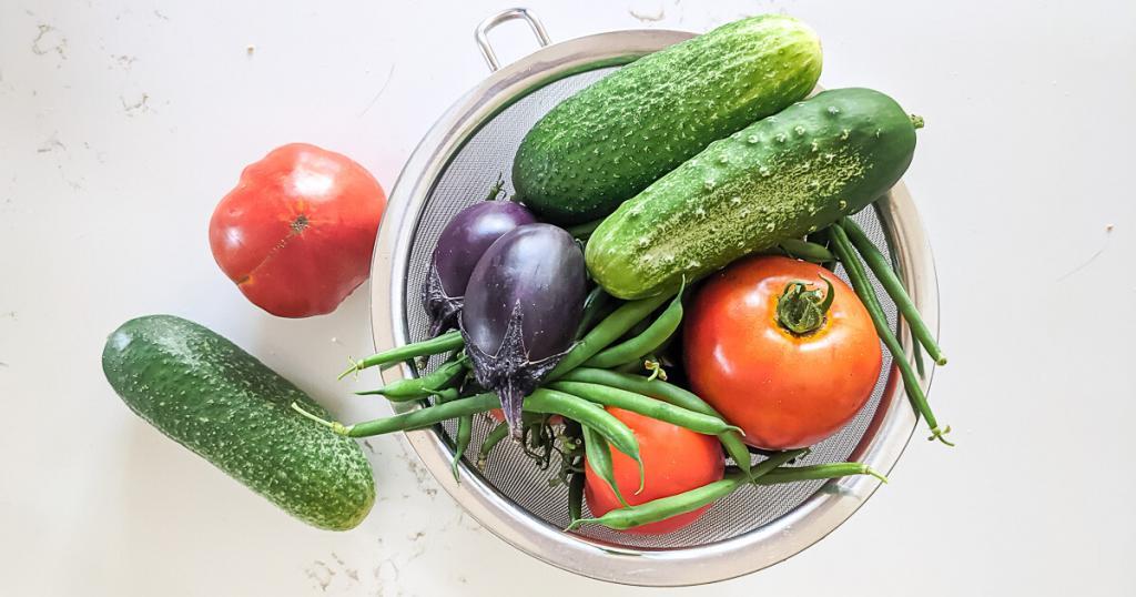 vegetables from the garden in a colander on a white counter.