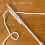 White Yarn cast on to knitting needles using the long-tail method.