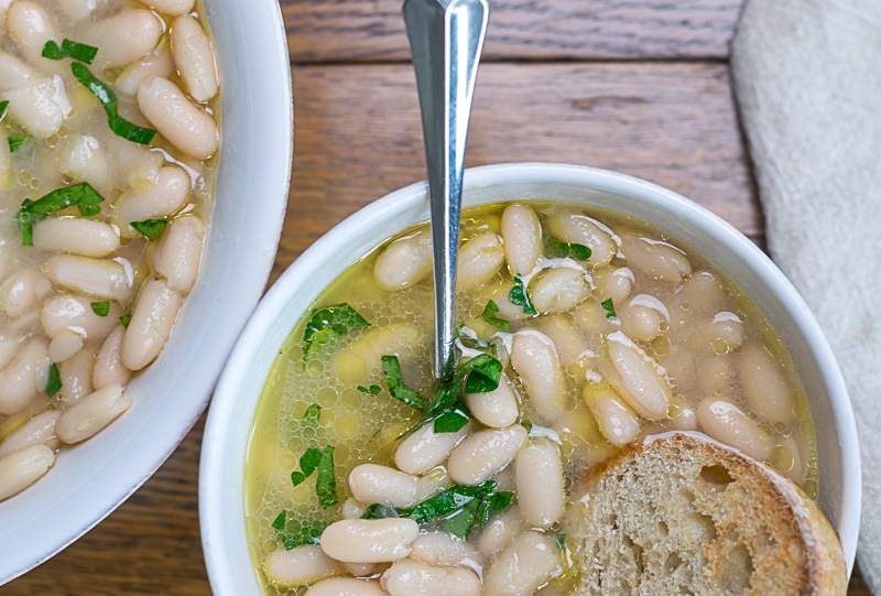 Brothy Beans in a white bowl; beans are a great grocery to buy on a budget.