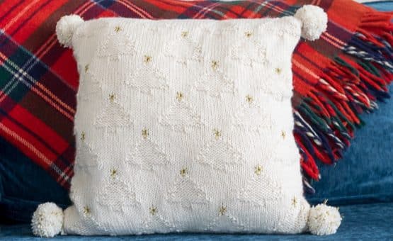 White knit pillow with white Christmas trees and gold stars.