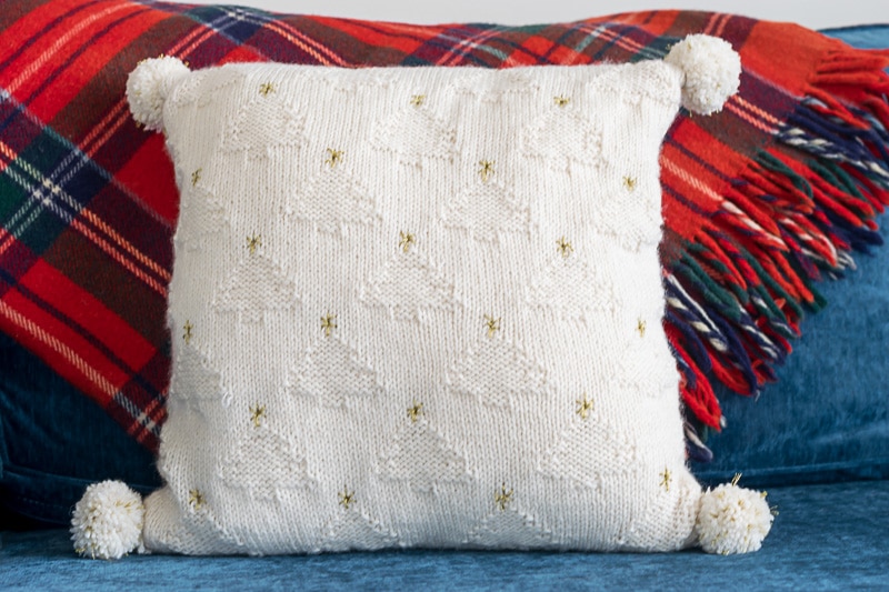 White knit pillow with white Christmas trees and gold stars.