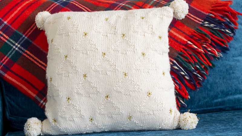 Christmas Tree Knit Pillow with plaid blanket in the background.