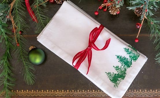 White Christmas napkins with green stamped Christmas trees and red ribbon.