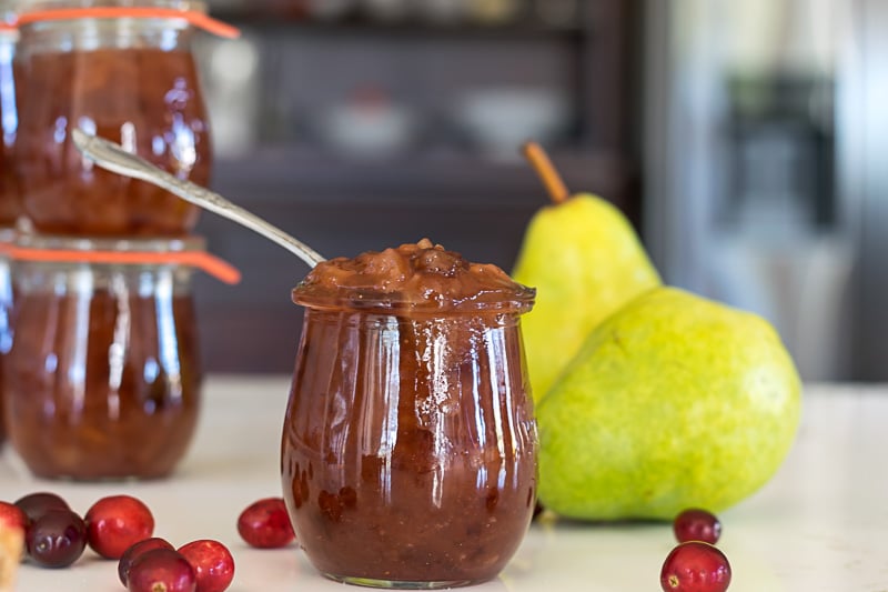 jar of jelly with fresh cranberries and pears in the background.