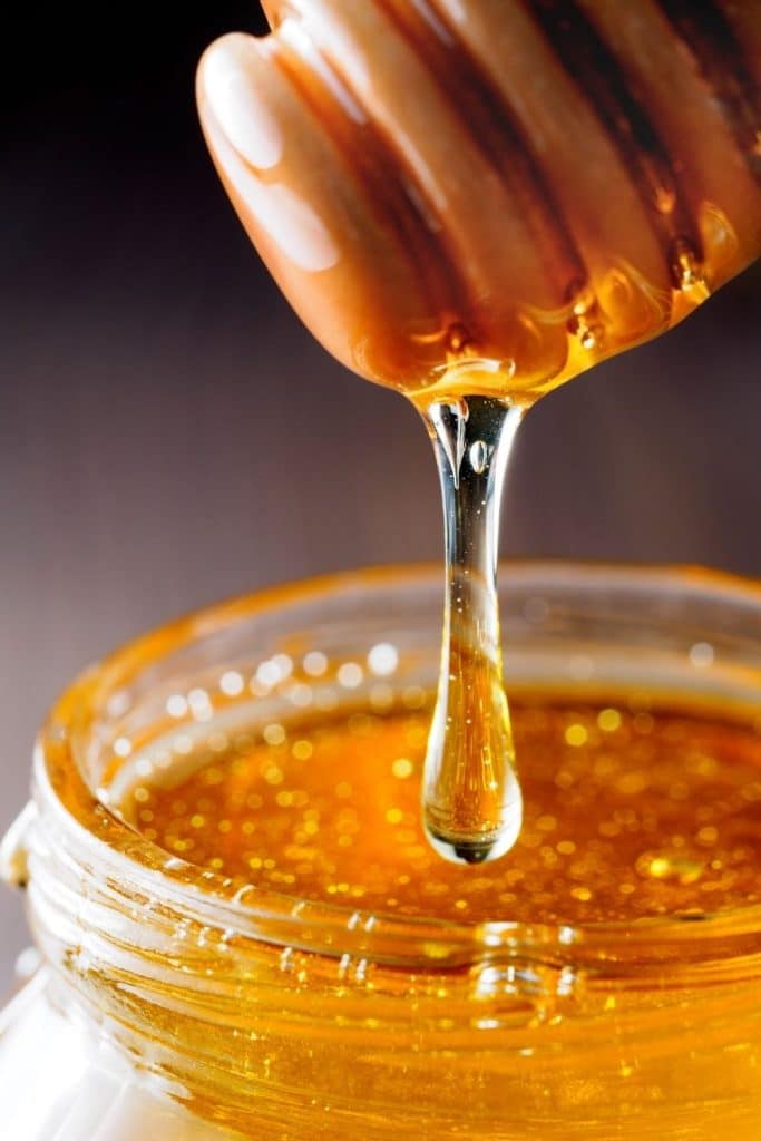 Honey dripping from honey stirrer into a jar.