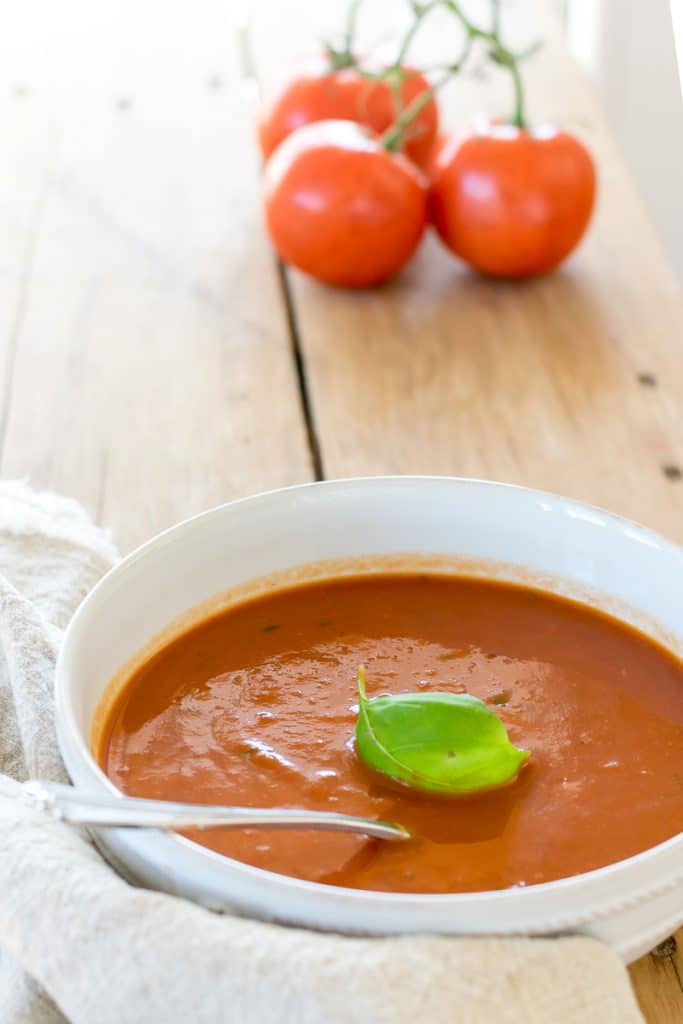 A bowl of  tomato soup with a basil leaf.