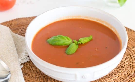 Bowl of Tomato soup with sprig of basil on top.