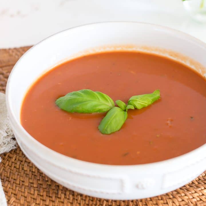 Bowl of Tomato soup with sprig of basil on top.