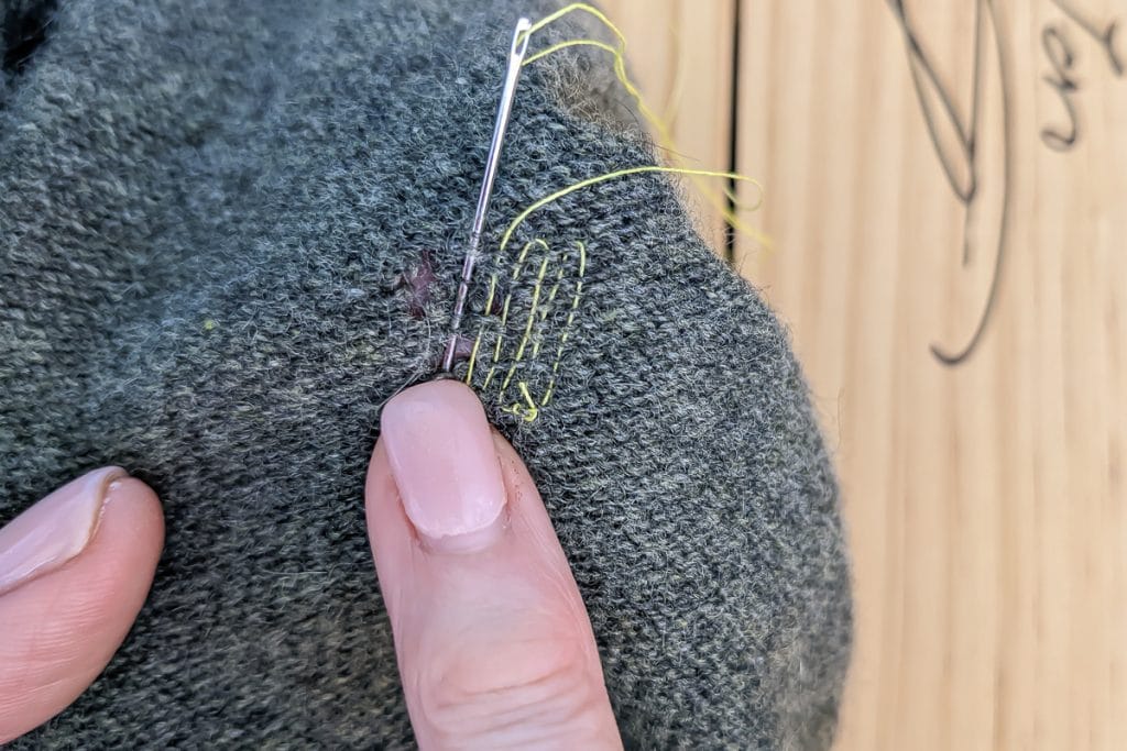Using needle and thread to mend a hole in knit fabric.