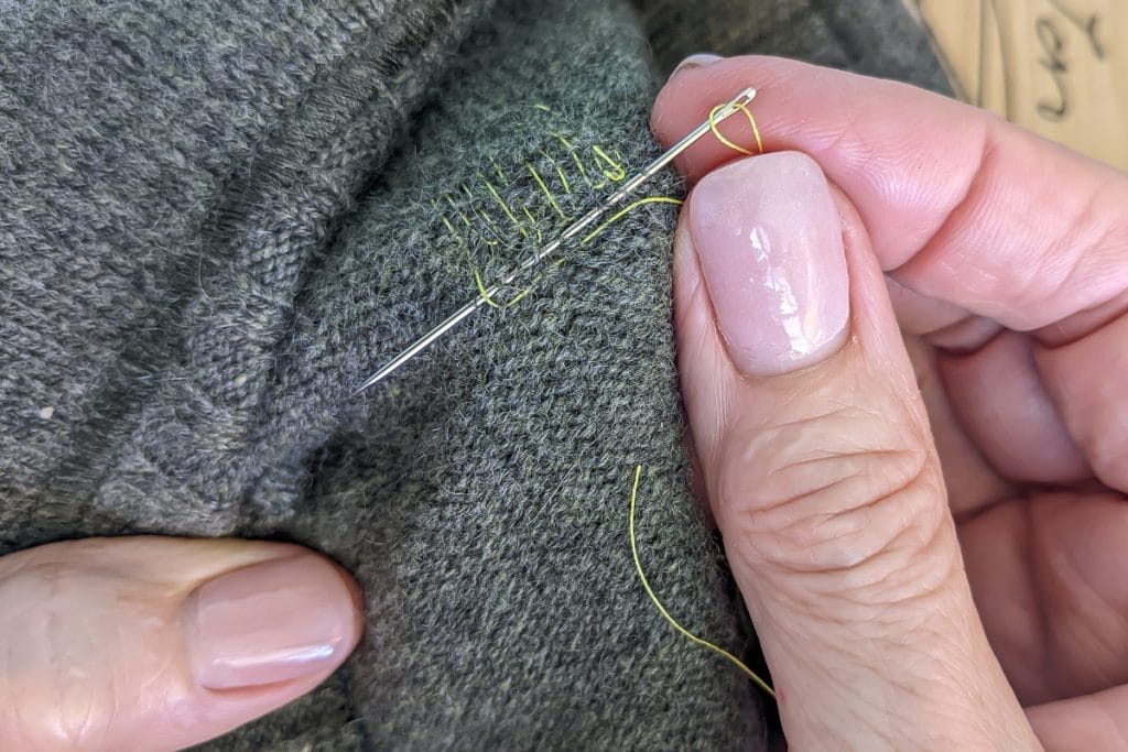 Using needle and thread to mend a hole in knit fabric.