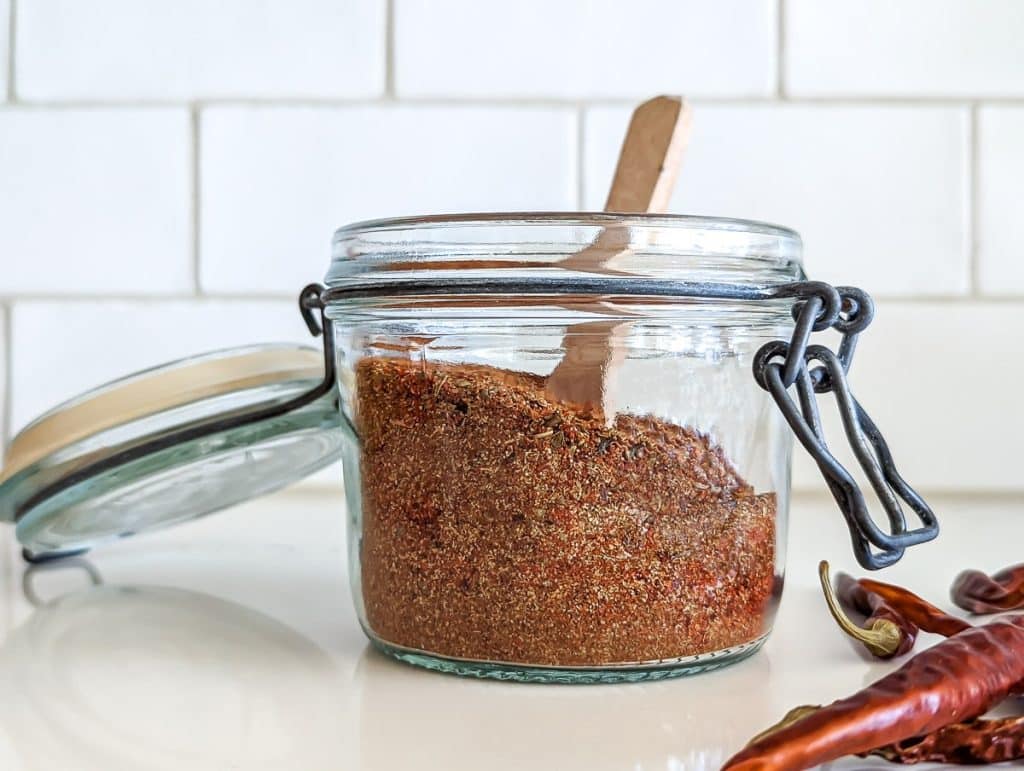 A glass jar with spices and a wooden spoon.
