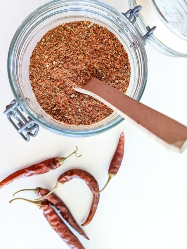 A jar of Smoky Chili Seasoning Recipe in a jar with chiles alongside.
